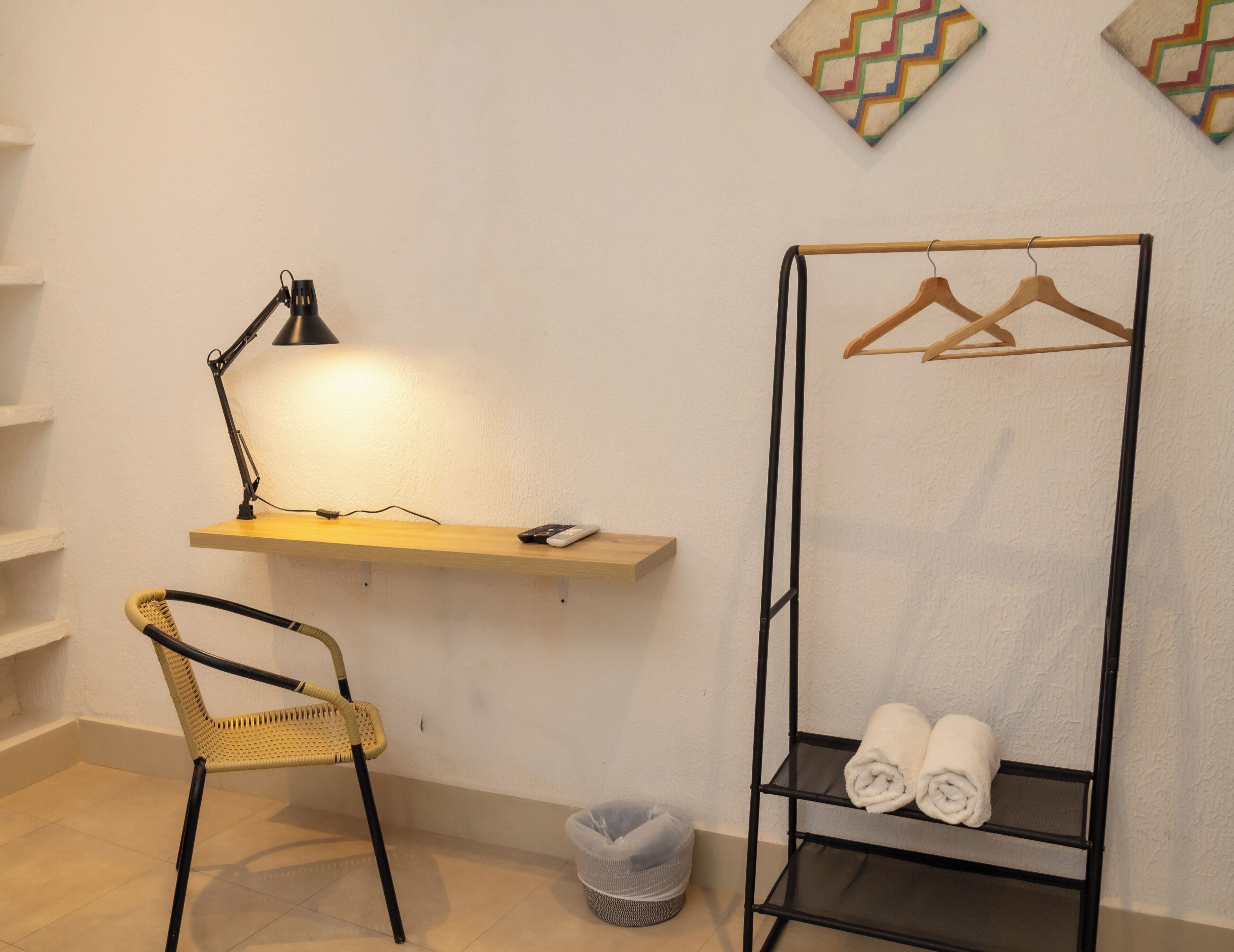 Ein Zimmer mit einem Sessel, einem Schreibtisch mit Lampe, einem Regal mit Handtüchern und einer Kleiderstange.