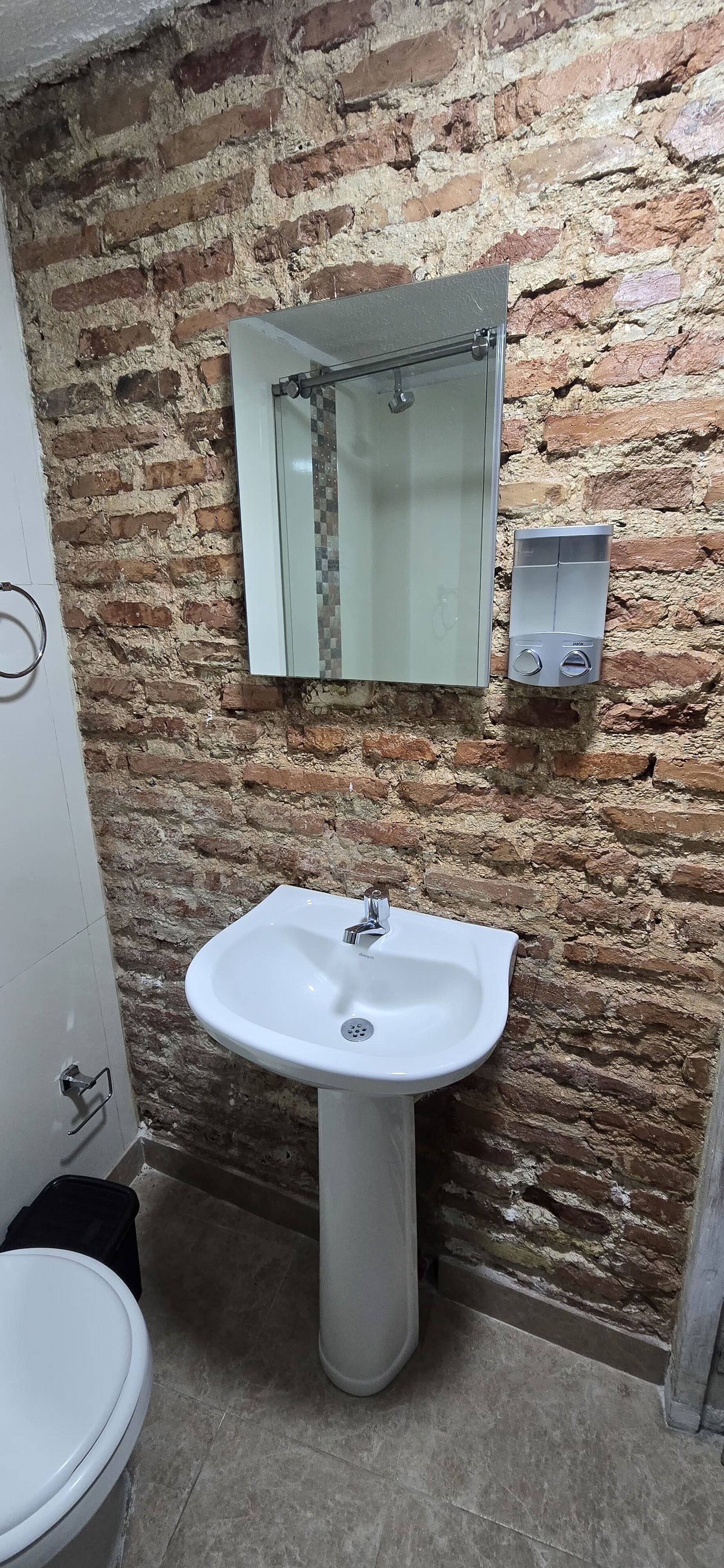 Un baño con un lavabo blanco, un espejo y una pared de ladrillo.