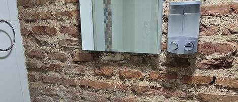 Un baño con un lavabo blanco, un espejo y una pared de ladrillo.