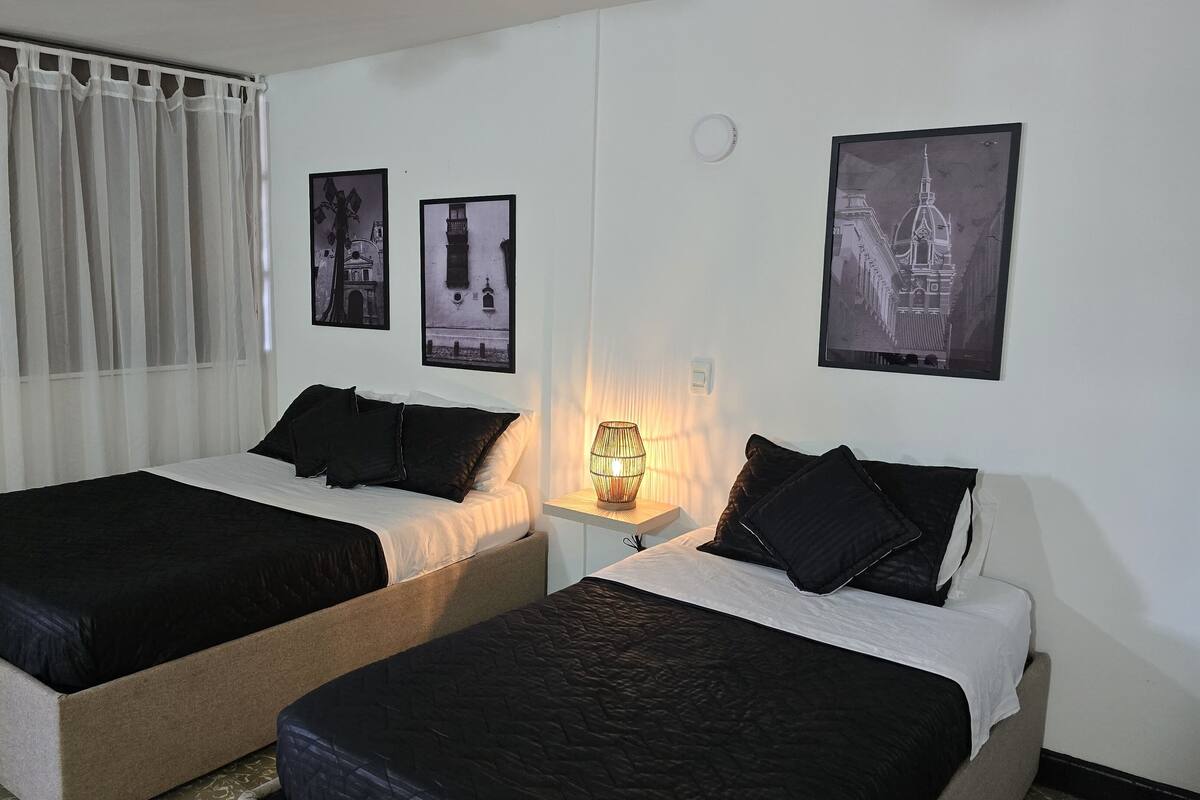 A hotel room with two beds, a nightstand with a lamp, and three framed pictures on the wall.