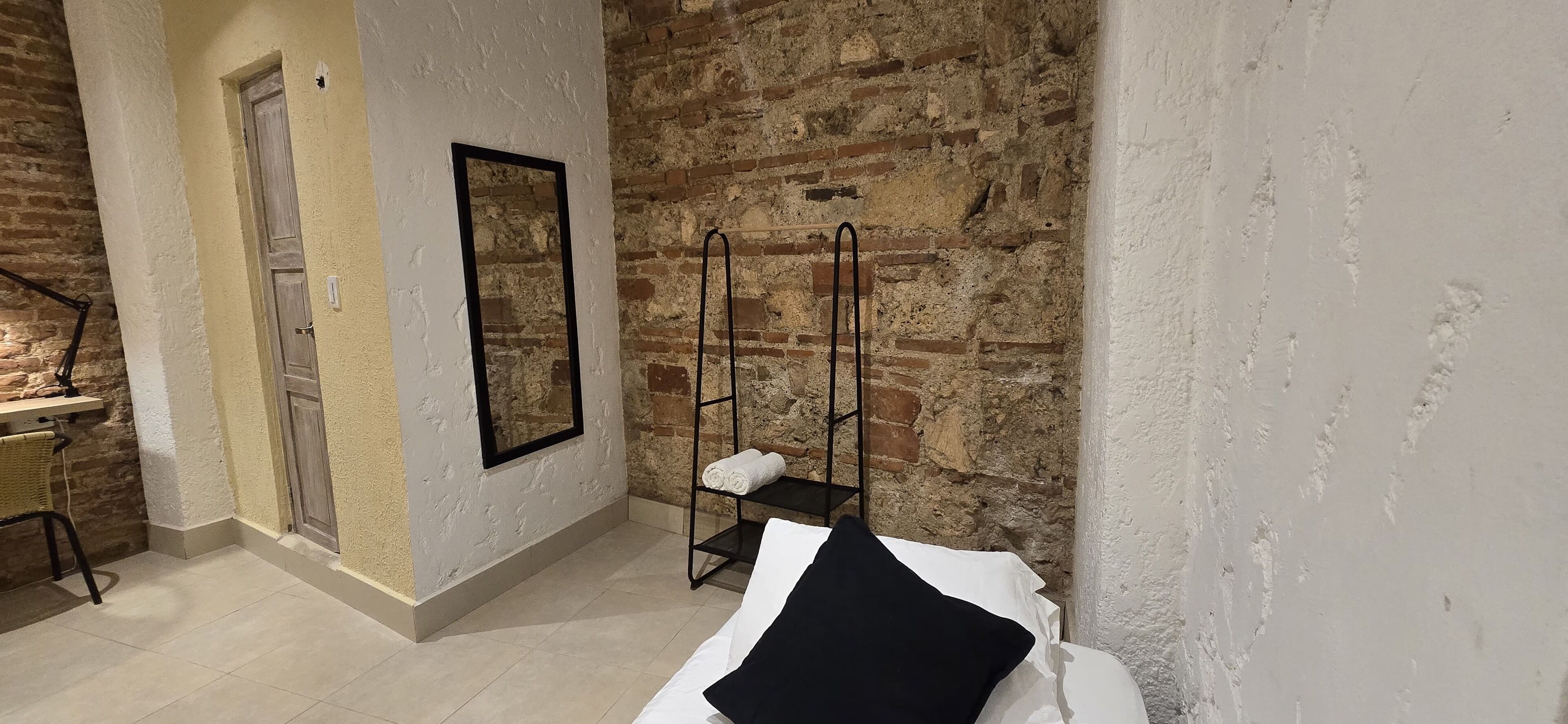 A room with a brick wall, a white door, a mirror, and a bed with white and black bedding.