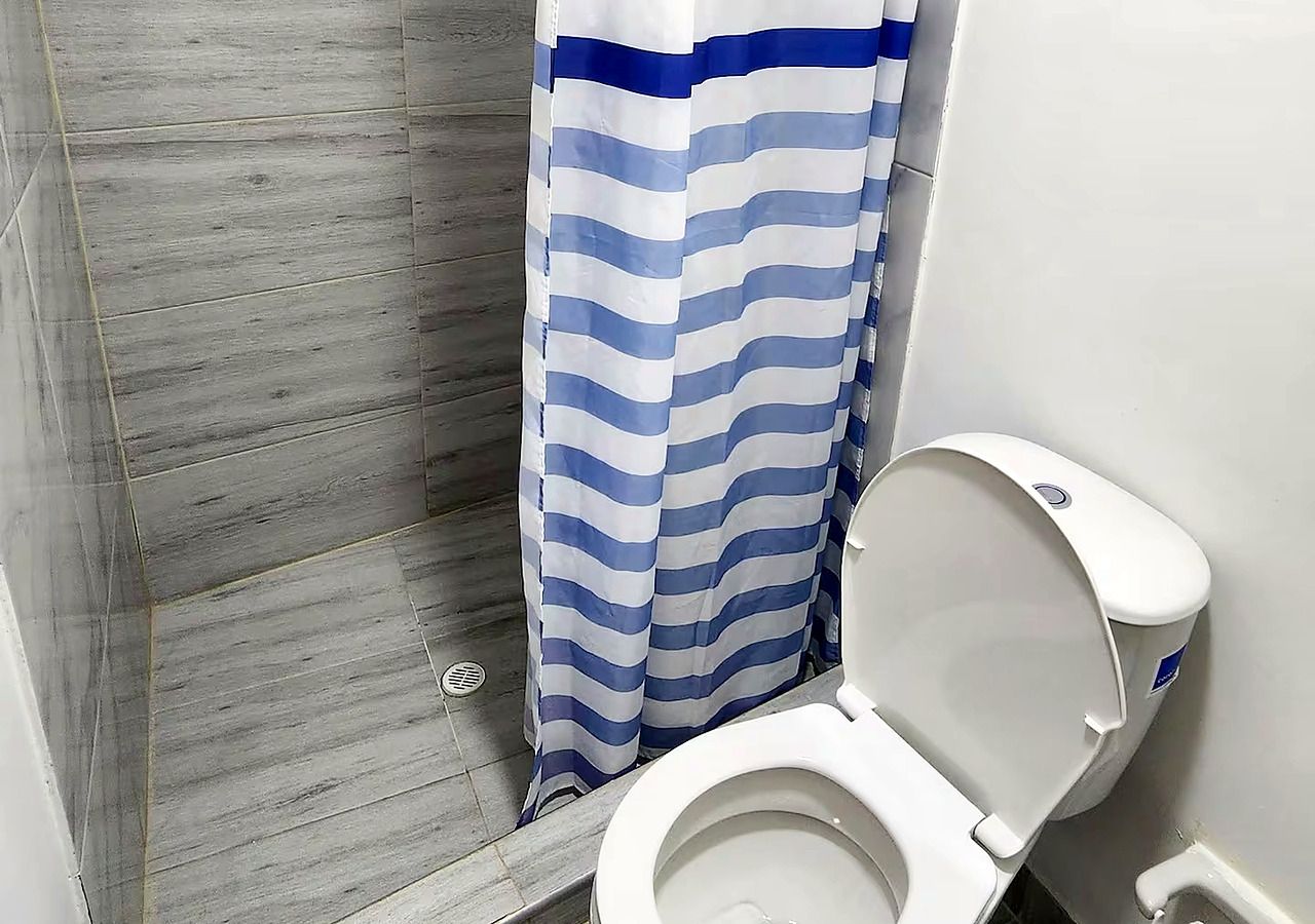 A bathroom with a white toilet, a shower with a blue and white striped shower curtain, and a wooden floor.