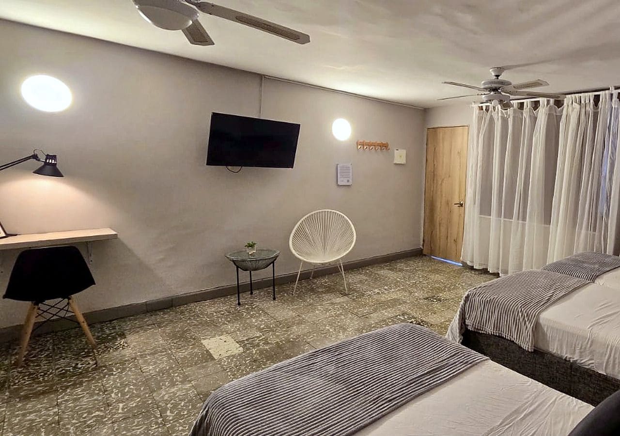 A hotel room with two beds, a desk, a chair, a television, and a ceiling fan.