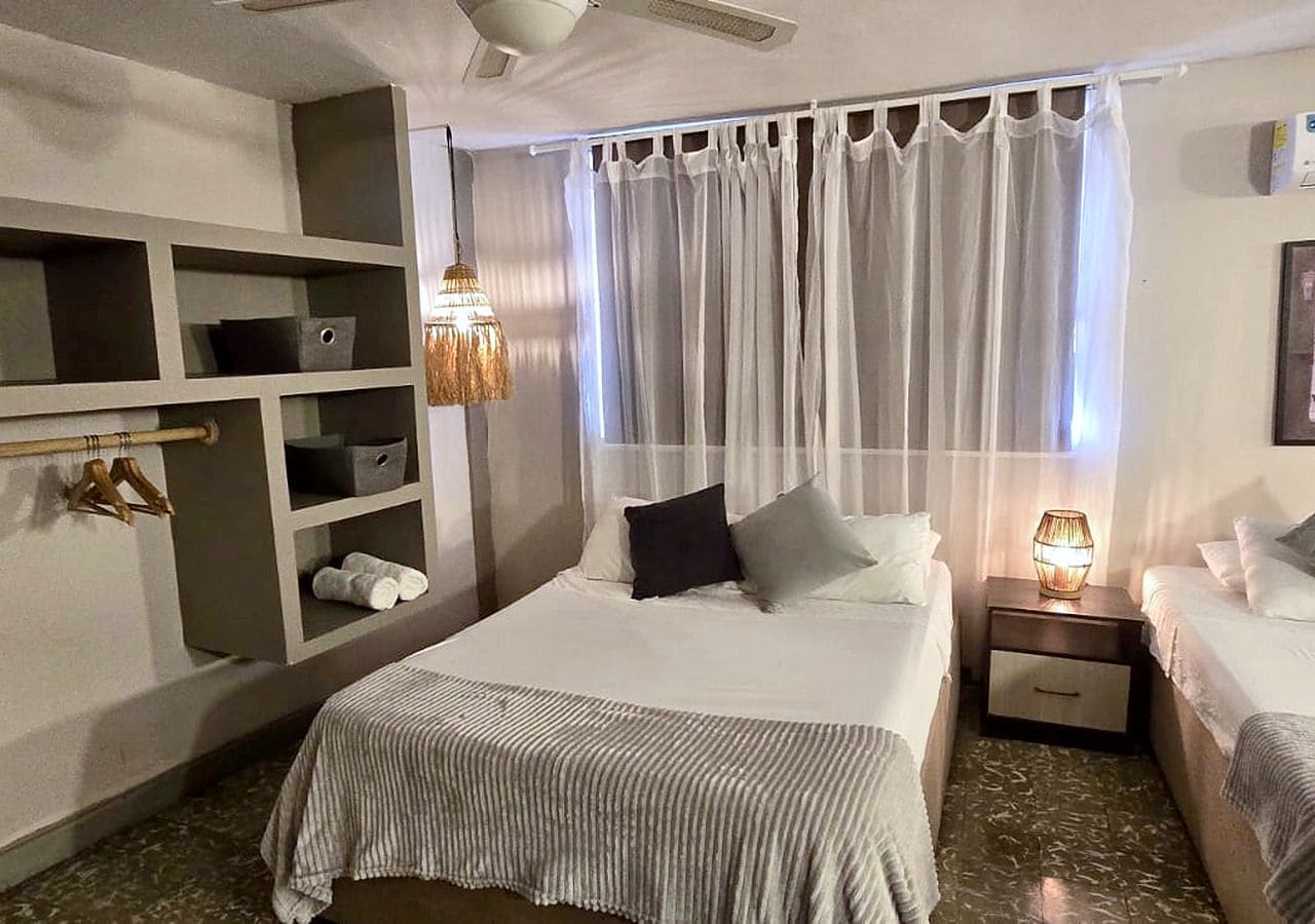 Habitación de hotel con cama, mesitas de noche, lámpara colgante y estantería empotrada.