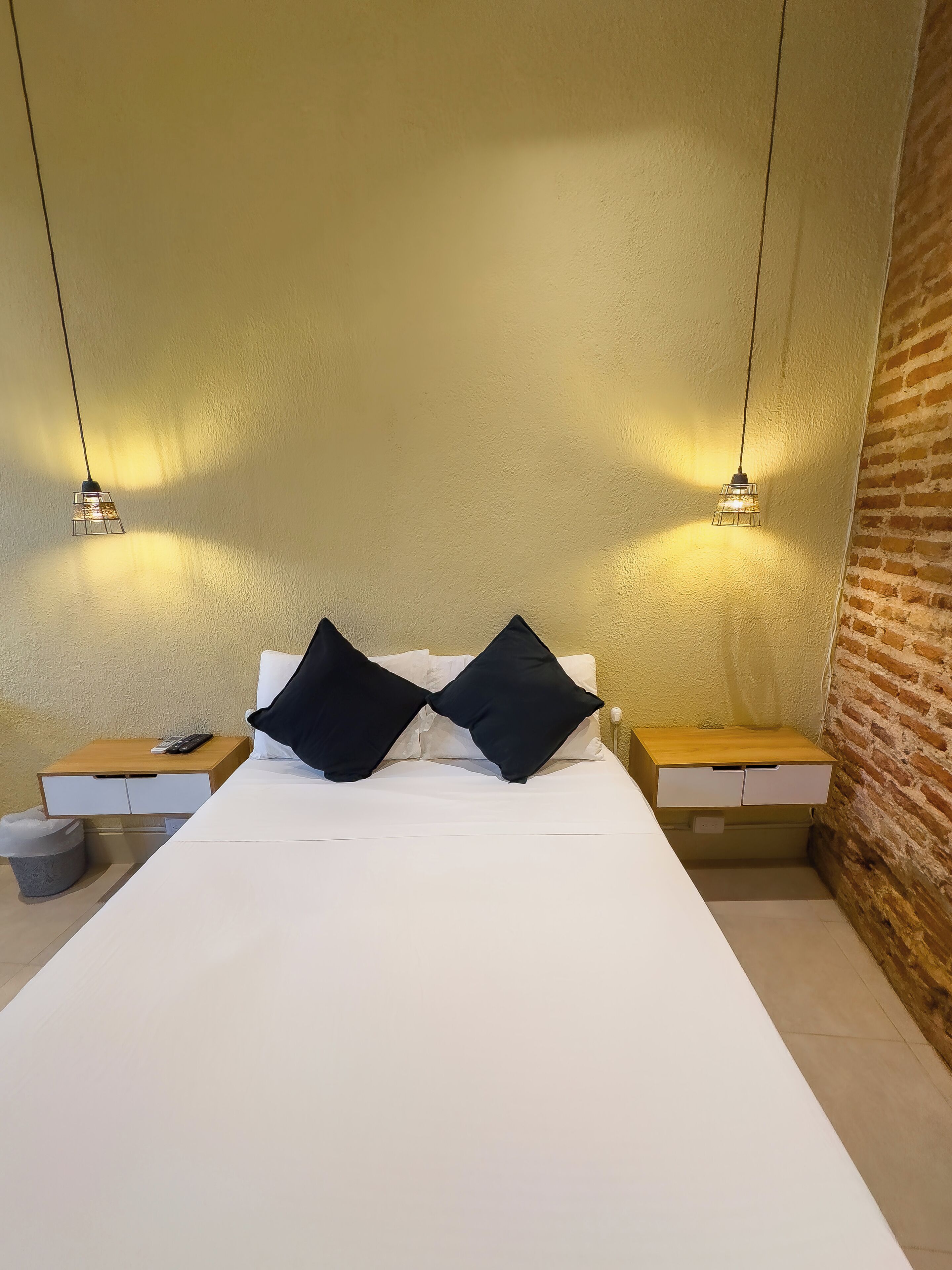 A minimalist hotel room with a large bed, two bedside tables, and a brick wall.