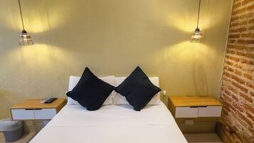 A minimalist hotel room with a large bed, two bedside tables, and a brick wall.