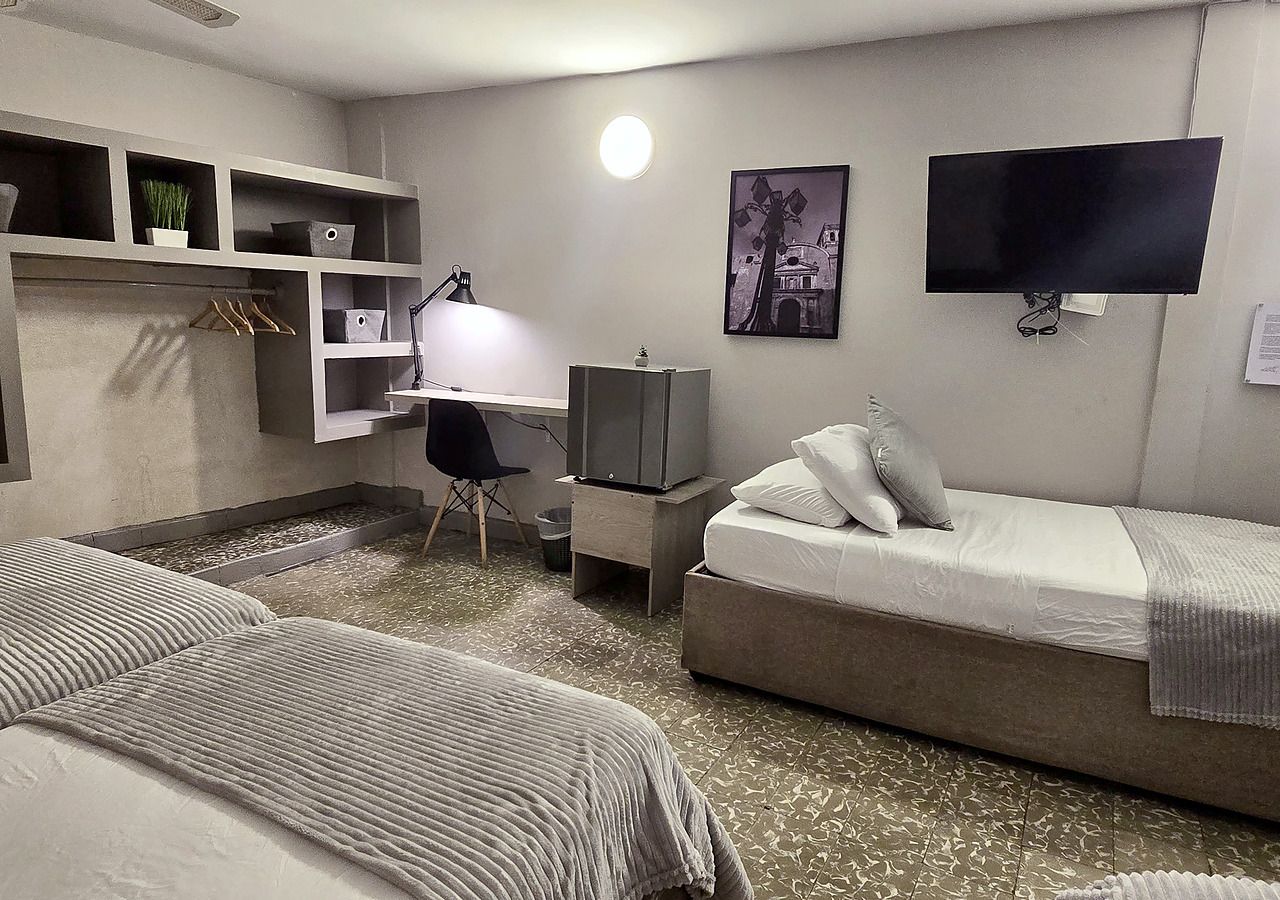 Une chambre d’hôtel comprenant un lit, un bureau avec une chaise, une télévision et une étagère avec des boîtes de rangement.