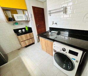 A compact kitchen with a washing machine, a microwave, and a coffee maker on the countertop.