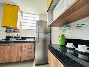 Een keuken met houten kastjes, een roestvrijstalen koelkast, een zwart aanrechtblad en een raam dat natuurlijk licht binnenlaat.