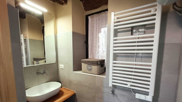 Un baño con un lavabo blanco, un espejo, un perchero para toallas y una ducha con persianas blancas.