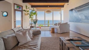 Ein geräumiges Wohnzimmer mit großem Fenster zum Meer, einem modernen Sofa und einer Holzbalkendecke.