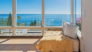 Ein Zimmer mit großem Fenster und Meerblick, einem Fellteppich und einem gestreiften Kissen.