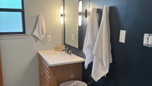 Une salle de bain équipée d’un lavabo, d’un miroir, d’un porte-serviettes et d’un panier à linge portant l’inscription « linge ».