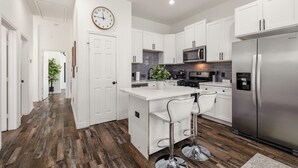 A modern kitchen with white cabinetry, a stainless steel refrigerator, and a central island with bar stools.