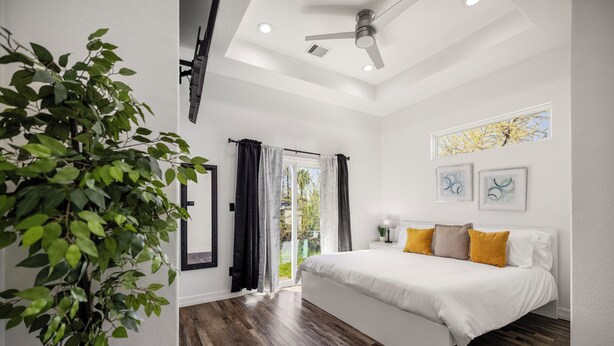 A bedroom with a bed, a ceiling fan, a window with curtains, and a plant.