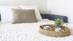 A bed with a white textured blanket, two pillows, a woven tray with a plant and two mugs, and a dark headboard. - Le Mirazur by Interhome (Nice)