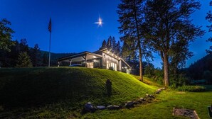 Una casa moderna en una colina cubierta de césped con una bandera, bajo un cielo estrellado.