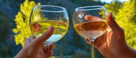 Deux mains tenant des verres à vin, avec un paysage montagneux en arrière-plan.