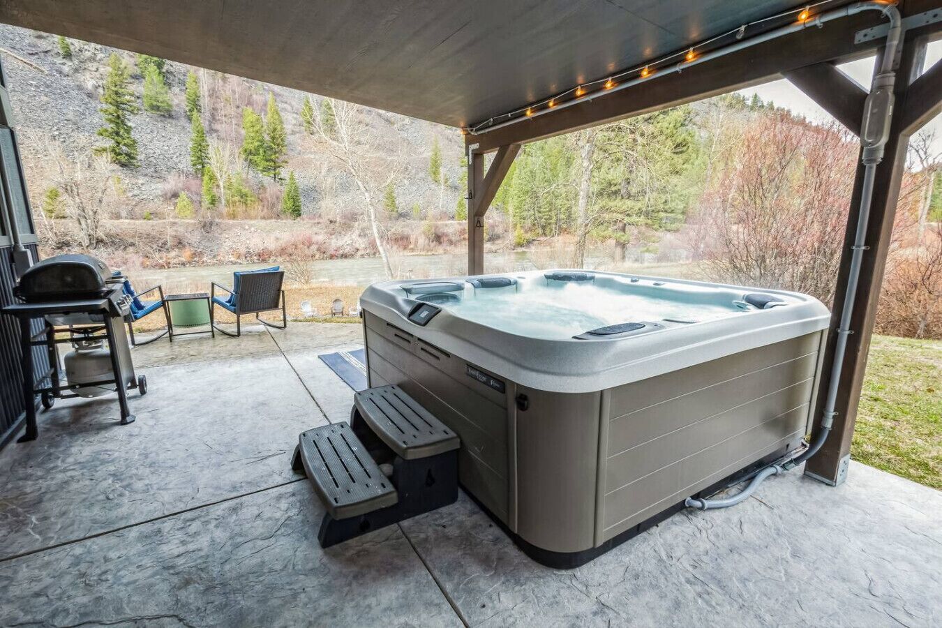 A hot tub under a covered patio with a view of a forested area.