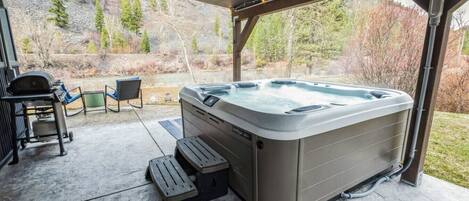 A hot tub under a covered patio with a view of a forested area.