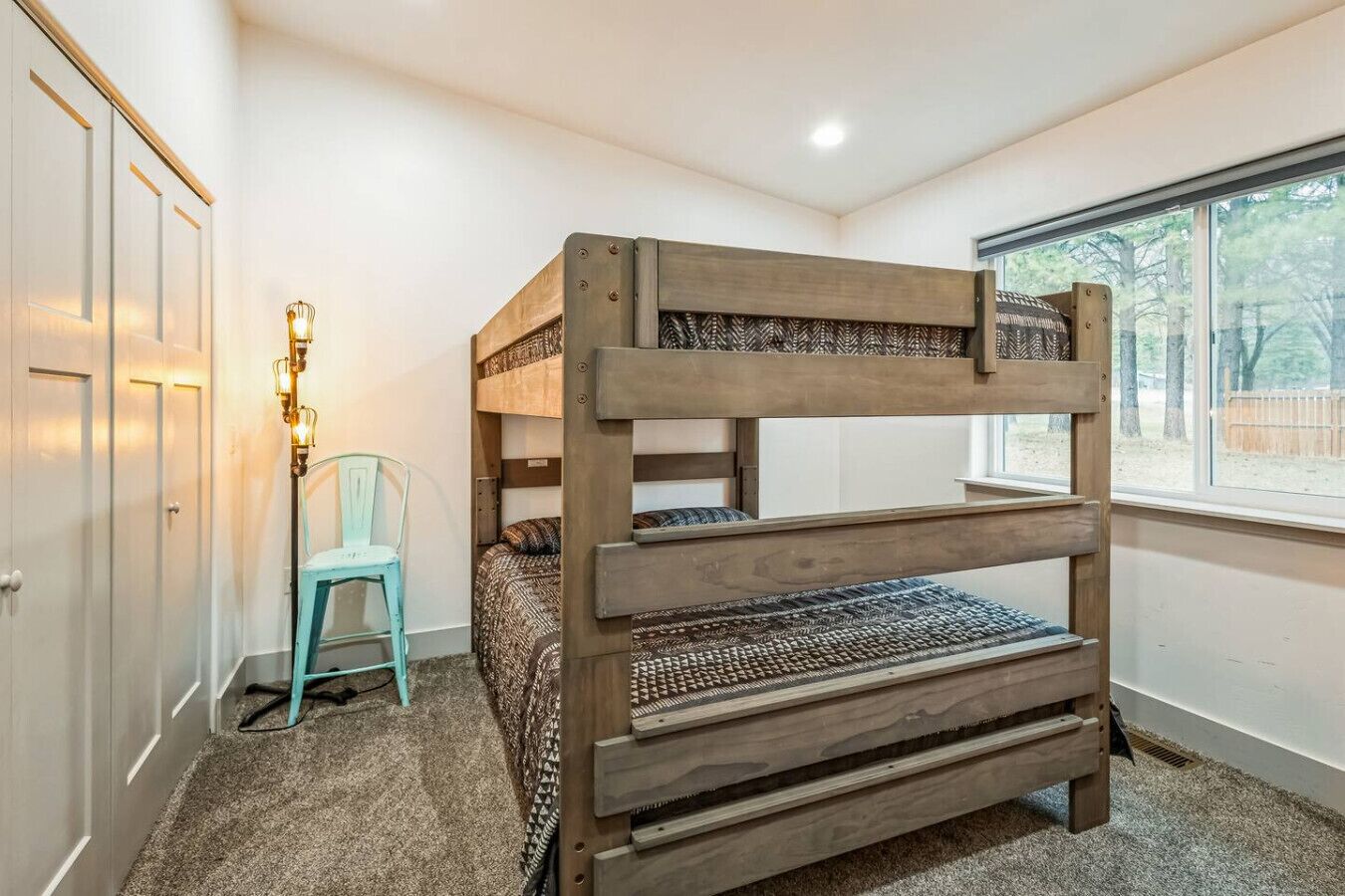A bunk bed in a room with a window, a chair, and a lamp.