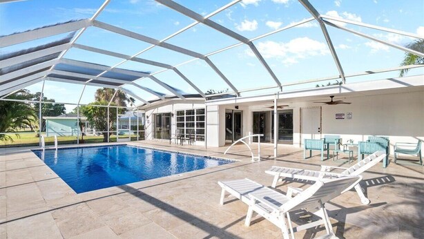 A covered swimming pool with lounge chairs, a ceiling fan, and a view of the surrounding area. - Mid-Century Modern Gem with Stunning Pool in PSL (Port St. Lucie)