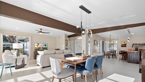A spacious living area with a dining table, blue chairs, and a ceiling fan. - Mid-Century Modern Gem with Stunning Pool in PSL (Port St. Lucie)