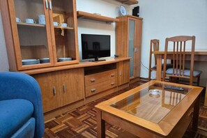 Un salon avec un téléviseur, des meubles en bois, une table basse en verre et un canapé bleu.