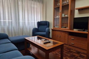A living room with a sofa, a blue armchair, a wooden coffee table, a cabinet with glass doors, and a television.