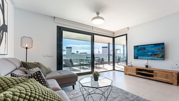 A modern living room with a sofa, a glass coffee table, and a TV on a wooden stand.