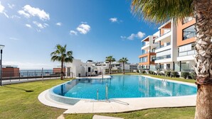 A modern pool area with a clear blue pool, surrounded by well-maintained grass and palm trees.
