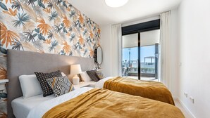A hotel room with a large bed, two bedside tables, a nightstand, a mirror, and a view of the outside balcony.