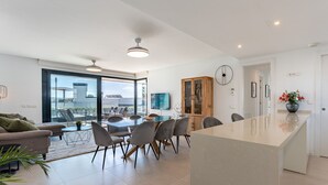 A modern kitchen with a central island, dining area with chairs, and a large window overlooking a terrace.