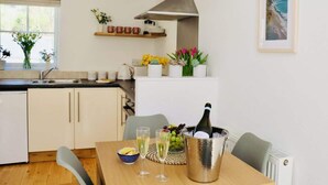 Une cuisine moderne avec des meubles blancs, une table à manger en bois et une bouteille de champagne.
