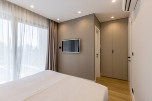 Une chambre à coucher moderne avec un grand lit, un téléviseur fixé au mur et une armoire.