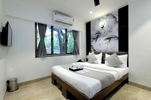 A modern hotel room with a large bed, a flat-screen TV, an air conditioning unit, and a view of trees through the window. - Myotel - Santacruz (Mumbai)