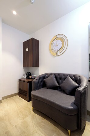 A modern living room with a dark brown sofa, a round wall clock, and a wooden cabinet. - Myotel - Santacruz (Mumbai)