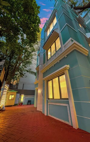 A two-story building with a light blue exterior, large windows, and a red brick pathway leading to the entrance. - Myotel - Santacruz (Mumbai)
