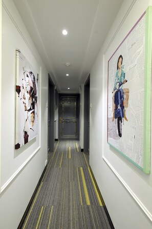 A hallway with artwork on the walls, a carpet with yellow lines, and a door labeled "302". - Myotel - Santacruz (Mumbai)