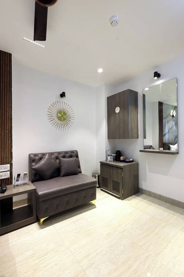 A modern bedroom with a grey sofa, a bedside table with a lamp, a small cabinet, and a wall-mounted mirror. - Myotel - Santacruz (Mumbai)