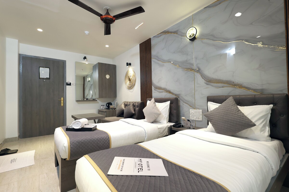 A hotel room with two beds, a ceiling fan, a marble wall, and a bedside table with a lamp.