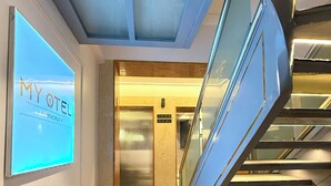 Un pasillo de hotel con piso de madera, techo con iluminación empotrada y un ascensor.