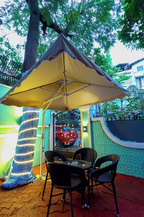 An outdoor seating area with a table and chairs under a canopy, a decorative tree trunk, and a wall with a mural. - Myotel - Santacruz (Mumbai)