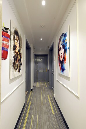 Un couloir d’hôtel avec des œuvres d’art accrochées aux murs, une moquette ornée de lignes jaunes et une porte au bout.