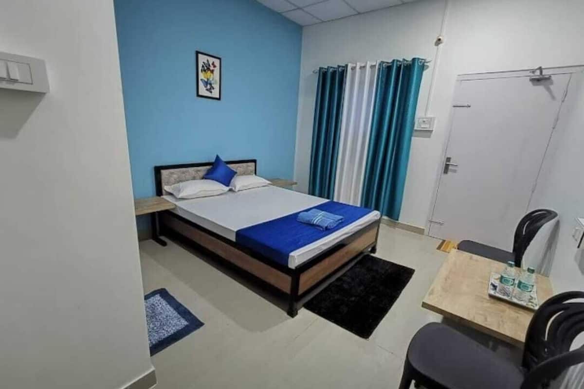 A bedroom with a bed, a desk, a chair, a door, and a curtain.