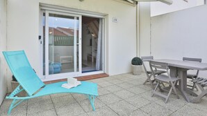 A balcony with a turquoise lounge chair, a table with chairs, and a sliding glass door leading to an interior space. - L'Échappée Chaumoise  Maison Cosy à 70m de la Plage (Les Sables-d´Olonne)