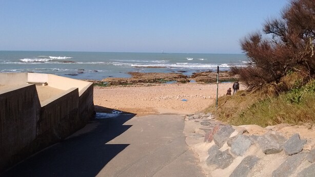 A coastal walkway leading to a beach with a rocky shoreline and a lighthouse in the distance. - L'Échappée Chaumoise  Maison Cosy à 70m de la Plage (Les Sables-d´Olonne)
