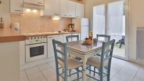 A kitchen with white cabinets, a tiled backsplash, a stove, and a dining table with chairs. - L'Échappée Chaumoise  Maison Cosy à 70m de la Plage (Les Sables-d´Olonne)