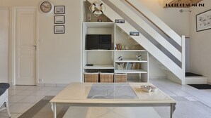 A living room with a sofa, a coffee table, a TV, and a staircase. - L'Échappée Chaumoise  Maison Cosy à 70m de la Plage (Les Sables-d´Olonne)