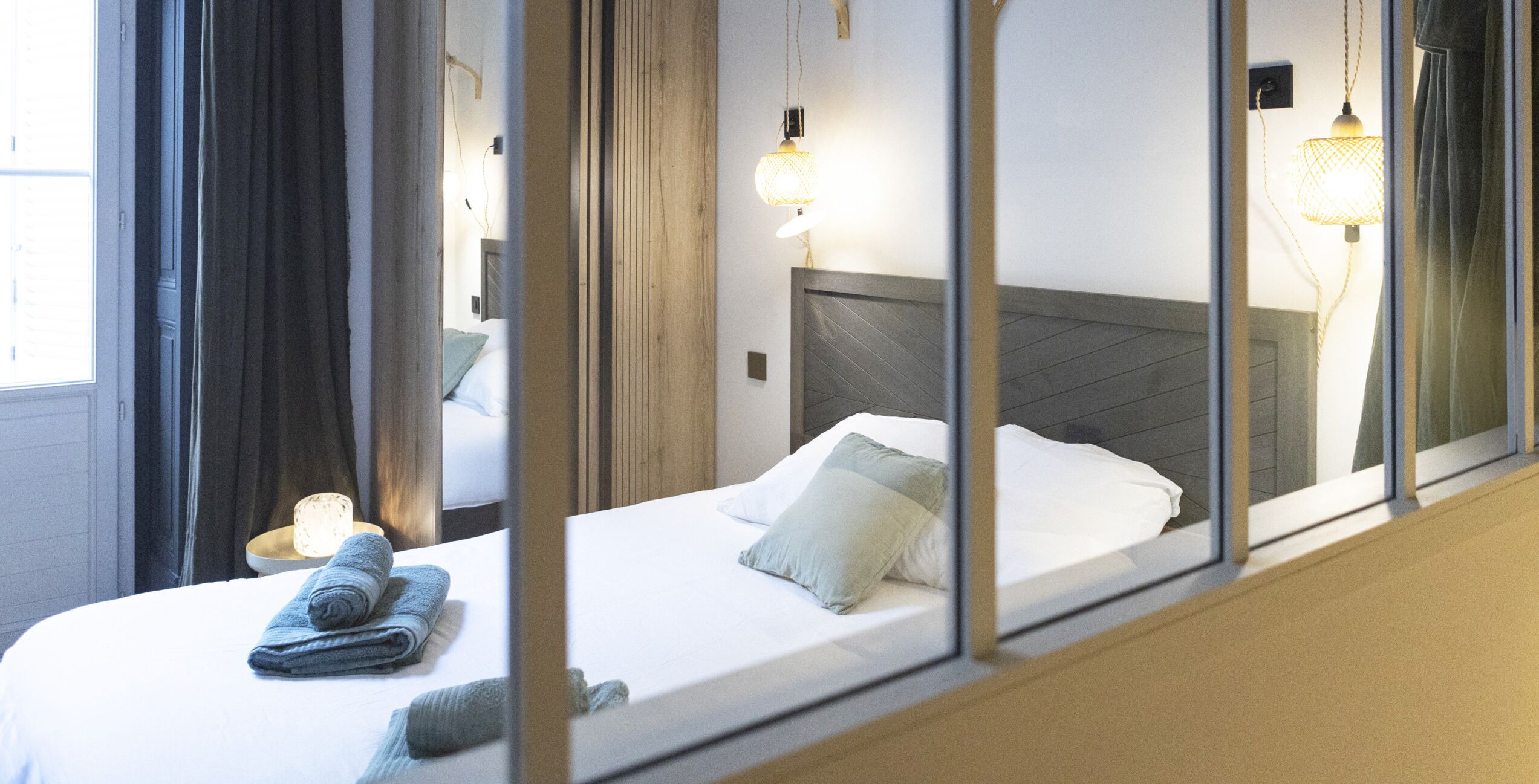 Habitació d'hotel amb llit, una tauleta de nit, una làmpada i una finestra amb cortines.